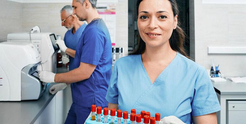 A female phlebotomy technician holds a tray of vials in a lab